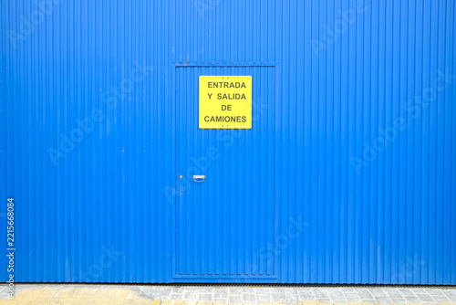 Minimalist blue corrugated metal wall with door and yellow truck entrance sign