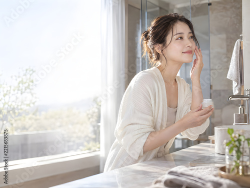 美容広告向け 洗面台でクリームをなじませる女性 透明感のある肌とナチュラルメイク 柔らかな朝の光と左側のコピースペース