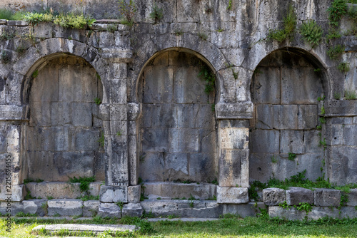 Close view of three rounded stone arches with weathered blocks and carved Armenian inscriptions and small plants growing along the ancient wall at Tatev Monastery, Tatev, Armenia