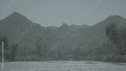 Green mountain slopes with trees and a wide flat riverbed in hazy daylight