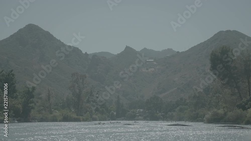 Misty mountains and green trees above a wide riverbed in morning light
