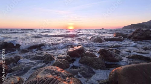 Sunset over rocky low tide shoreline with shimmering surf and warm orange sky reflecting on wet boulders timelapse