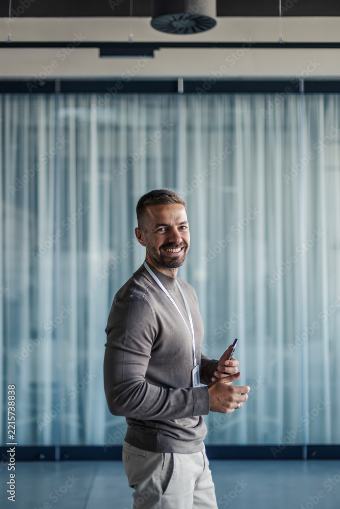 Fototapeta premium Smiling man standing in modern office holding phone