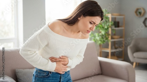 Woman clutching stomach in pain at home with neutral expression