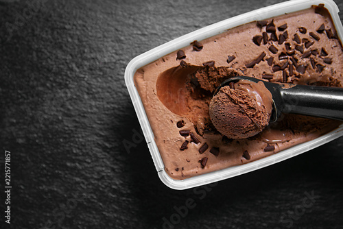 Chocolate ice cream with chocolate chips in a plastic container, photographed from above on a dark textured background.