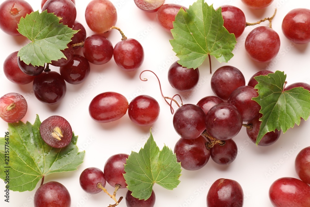 Fototapeta premium Fresh ripe grapes and green leaves on white background, flat lay
