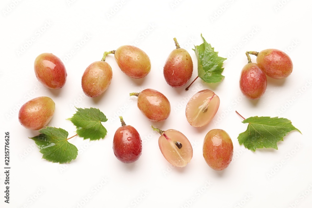 Fototapeta premium Fresh ripe grapes and green leaves on white background, flat lay