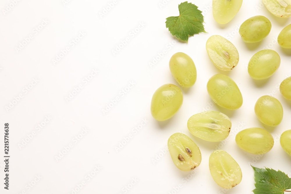 Naklejka premium Fresh ripe grapes and green leaves on white background, flat lay. Space for text