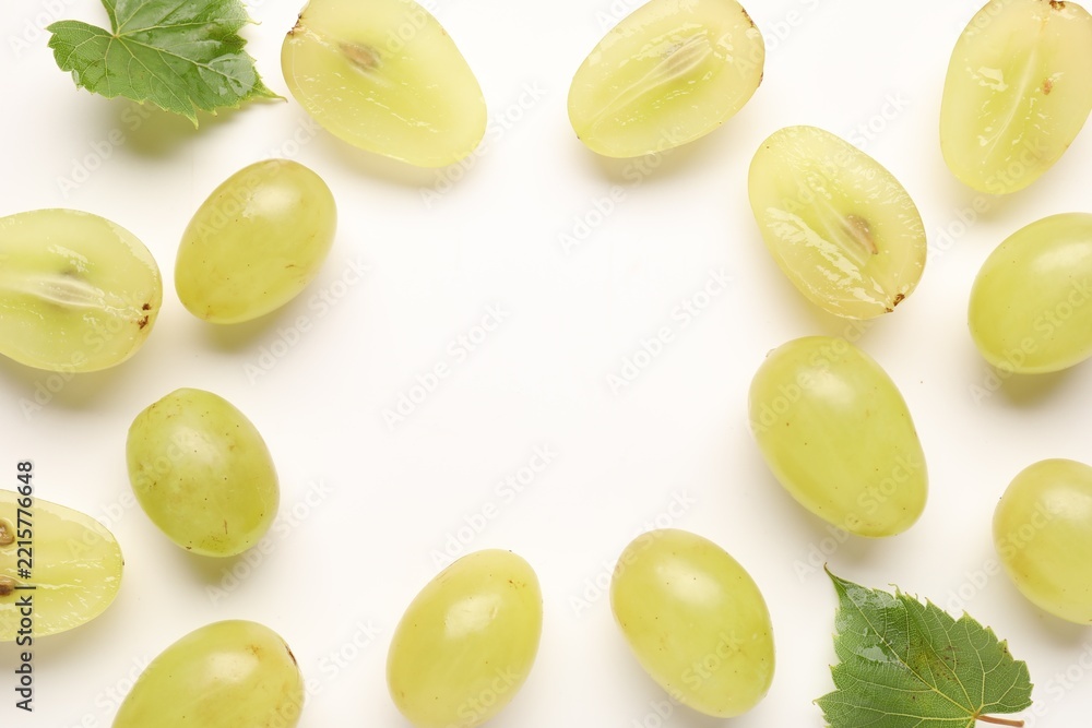 Naklejka premium Fresh ripe grapes and green leaves on white background, flat lay. Space for text