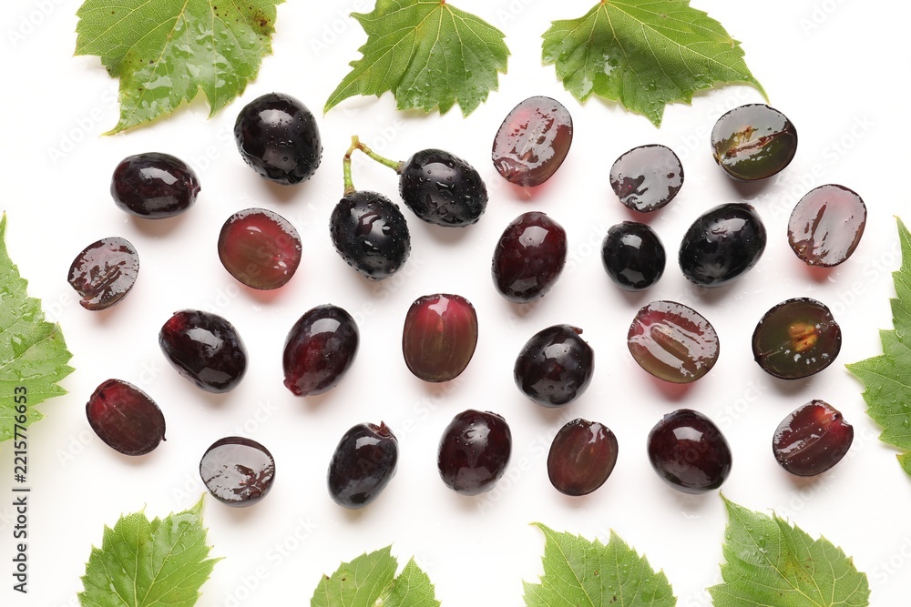 Fototapeta premium Fresh ripe grapes and green leaves on white background, flat lay
