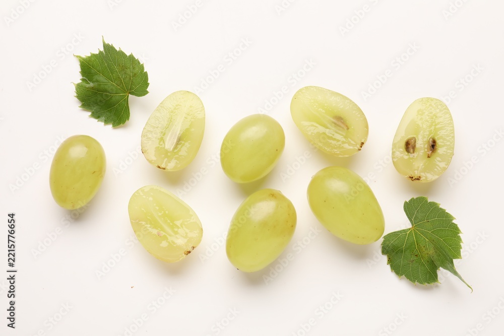 Naklejka premium Fresh ripe grapes and green leaves on white background, flat lay