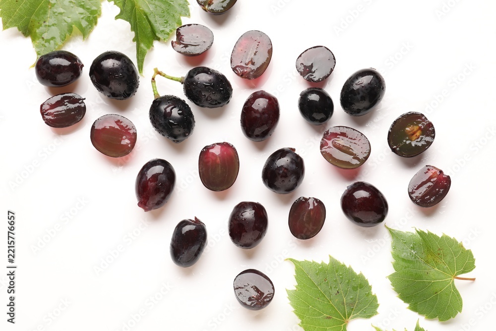 Fototapeta premium Fresh ripe grapes and green leaves on white background, flat lay