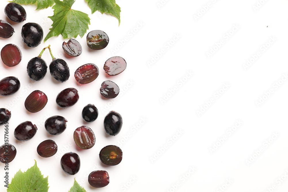 Fototapeta premium Fresh ripe grapes and green leaves on white background, flat lay. Space for text
