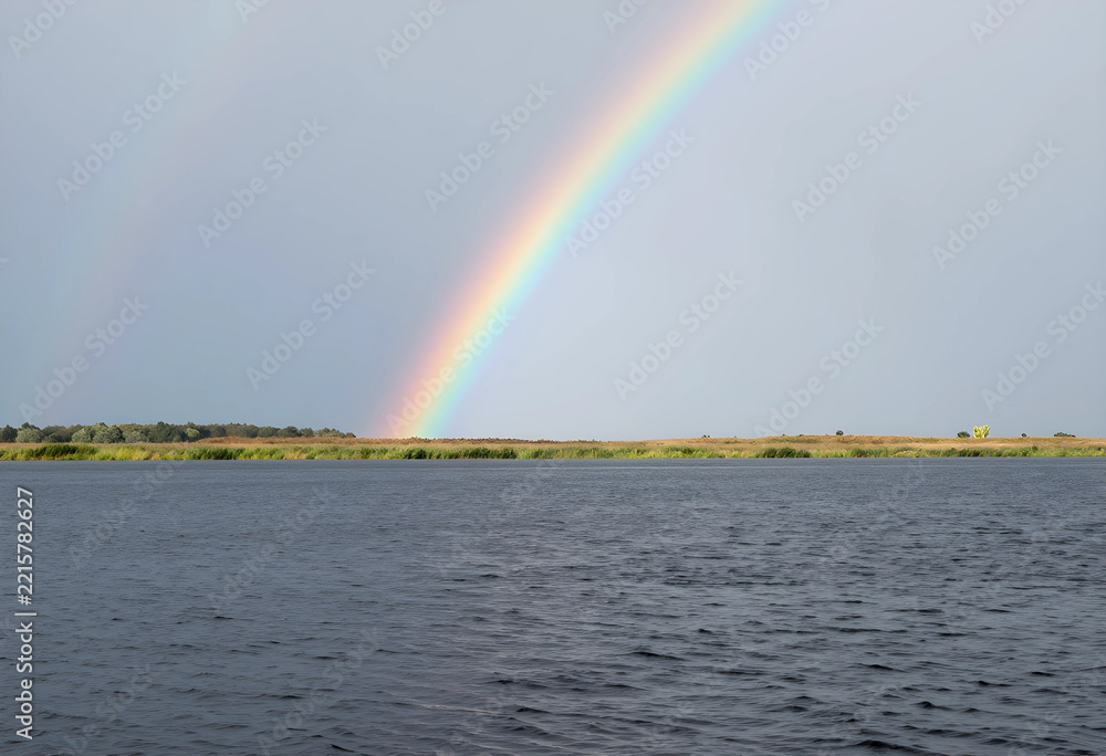 Naklejka premium Hope and optimism concept, bright rainbow over a calm lake landscape with grassy horizon after a storm, weather phenomenon in nature and environment
