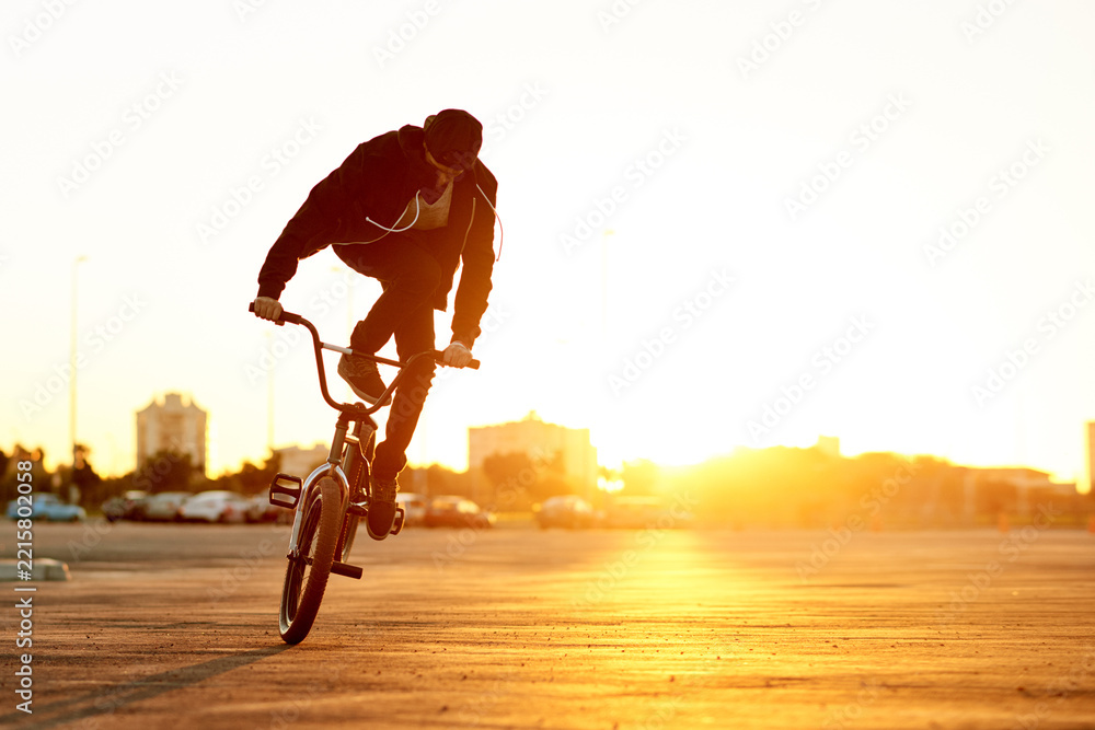 Naklejka premium City, sunset and trick with man on BMX for adrenaline, exercise or extreme sports outdoor. Bike, flare and training with rider on asphalt street in urban town for action, hobby or skill practice