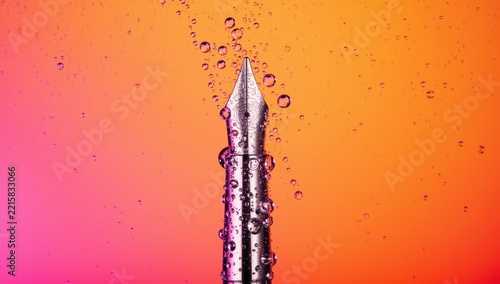 Elegant Silver Fountain Pen Nib with Glistening Water Droplets on a Vibrant Pink and Orange Gradient Background
