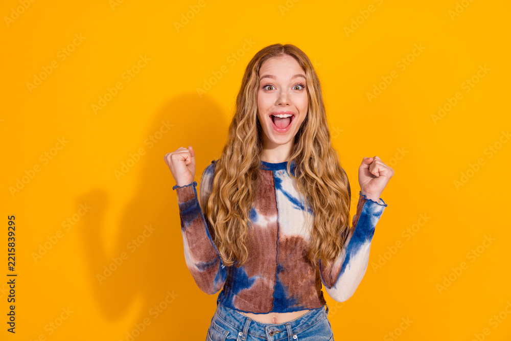 Fototapeta premium Young woman with blonde hair wears a tie dye top and celebrates with a smile against a bright yellow background