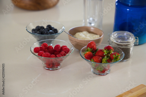 Three glass bowls are sitting on light countertop with raspberries, strawberries, blueberries