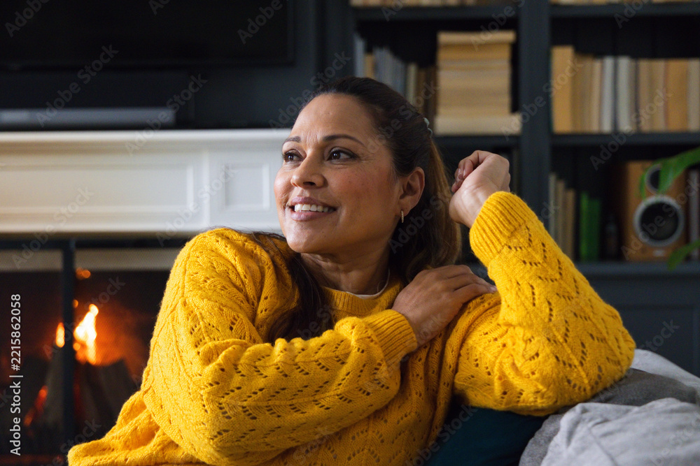 Naklejka premium Middle-aged African woman resting on couch by lit fireplace, wearing mustard sweater