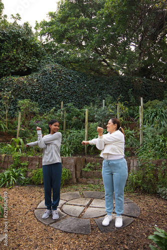 African American mom and teenage daughter stretching on stone patio in athletic wear and sneakers