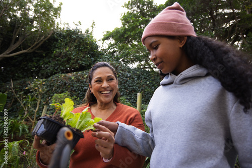 African American mother and teen smiling holding black seedling tray in rust sweater tending garden