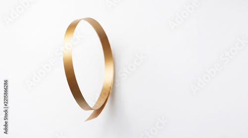 Single gold ribbon twisted into a loop on a white background, keywords: gold, ribbon, loop