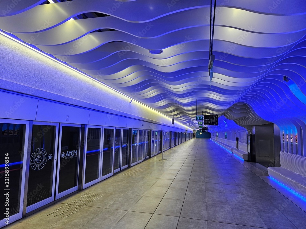 Fototapeta premium ISTANBUL - APR 10, 2026: Modern subway station with blue-lit wavy ceiling. Glass doors line the platform. Bright lights illuminate the curved architecture. Clean, sleek, and futuristic design