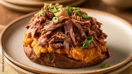 Loaded baked potato topped with pulled pork, cheese and green onions on ceramic plate, comfort food catering and barbecue menu concept