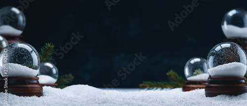 Christmas snow globes with pine tree branches on a snowy surface against a dark blue background with copy space
