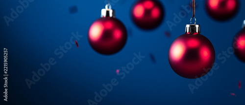 Red Christmas ornaments hanging against a deep blue background with festive bokeh light effects