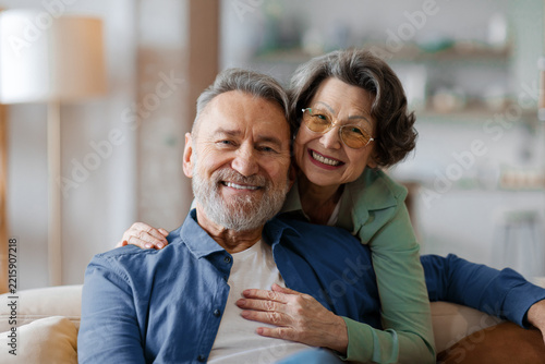 Smiling senior couple posing affectionately on sofa at home