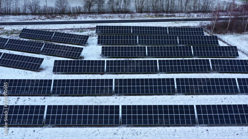 Aerial view of a solar farm with rows of photovoltaic panels installed in a snowy field in Latvia.