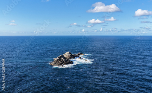 Aerial view of a rocky outcrop surrounded by deep blue ocean waters under a clear sky in Byron Bay, New South Wales, Australia.