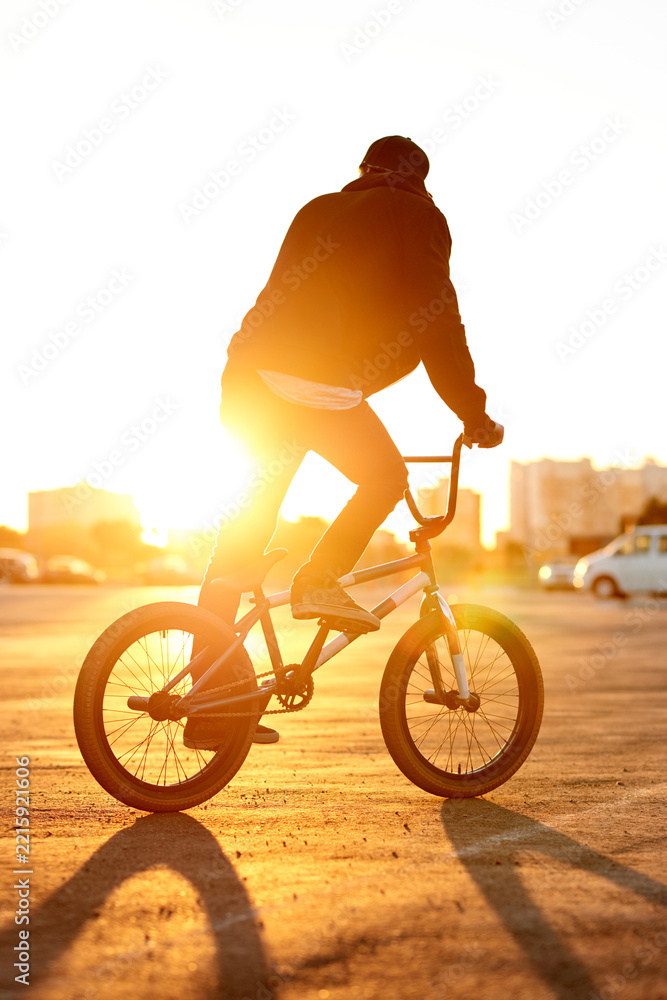 Naklejka premium Balance, city and sunset with man on BMX for adrenaline, exercise or extreme sports outdoor. Bike, flare and training with rider on street in urban town for action, hobby or practice from back