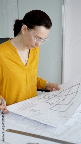Architect woman reviewing and working on blueprints in office, designing new building construction plans, focusing on engineering details and planning project development