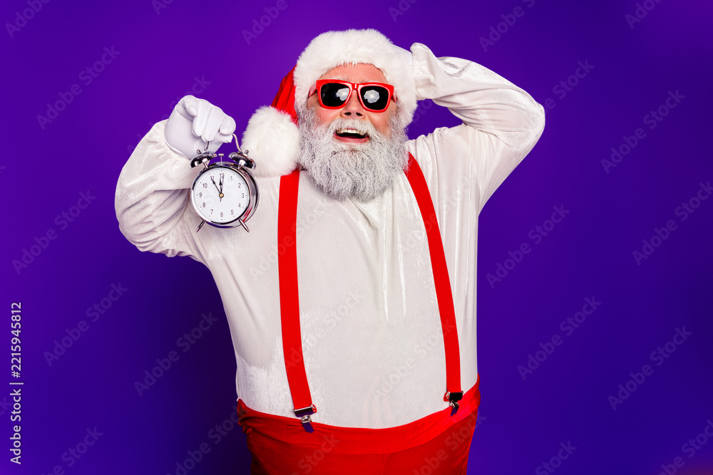 Fototapeta premium Santa Claus holding an alarm clock for Christmas countdown, smiling in red suspenders and sunglasses against a purple background
