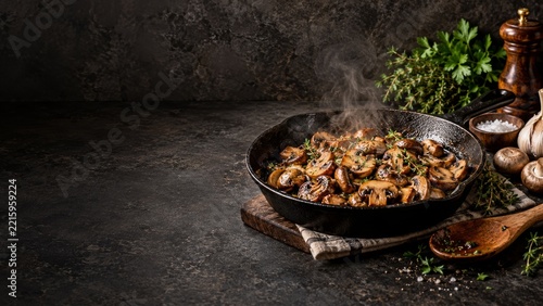 Steaming mushroom skillet with garlic and herbs on a dark kitchen counter