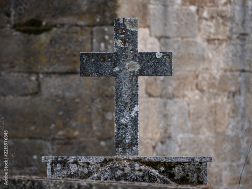 Detail view of a stone cross on a pedestal of the same material but deteriorated by the passage of time on top of a tomb in the door of a church