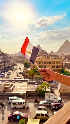 Hand holding Egyptian flag overlooking street traffic and the Great Pyramids of Giza