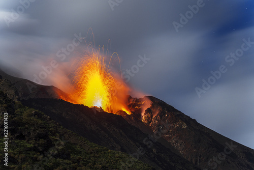 Aerial view of the Stromboli volcano erupting with glowing lava fountains and volcanic ash against a dark twilight sky, Lipari, Sicily, Italy.