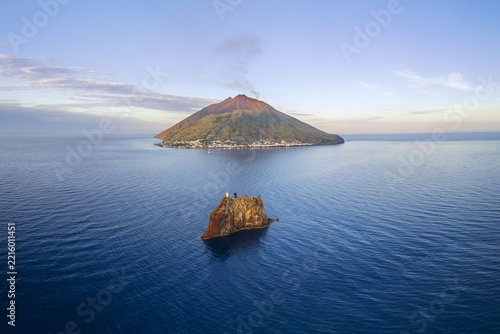 Aerial view of the Stromboli volcano emitting smoke above the Tyrrhenian Sea with a rocky islet in the foreground near Lipari, Sicily, Italy.