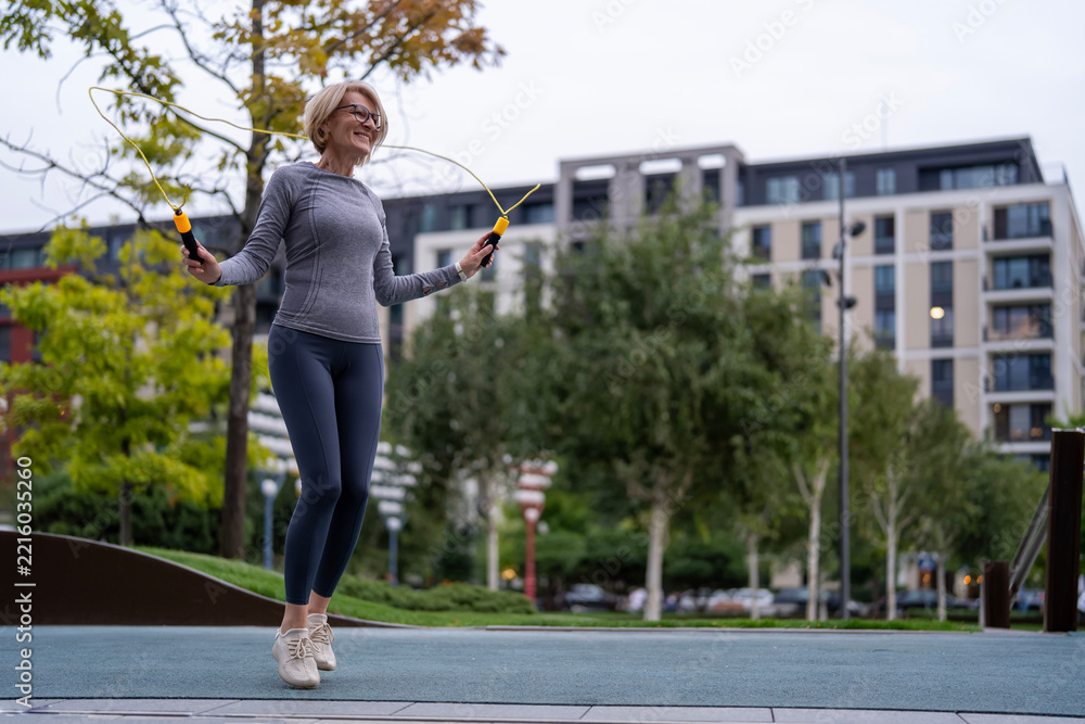 Fototapeta premium Happy senior woman exercising jumping rope outdoor