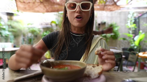 Young woman eating soup with bread at outdoor cafe patio under soft daylight