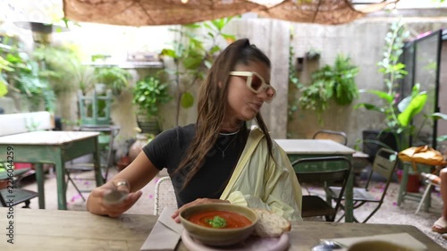 Woman eating red soup at outdoor cafe table wearing white sunglasses