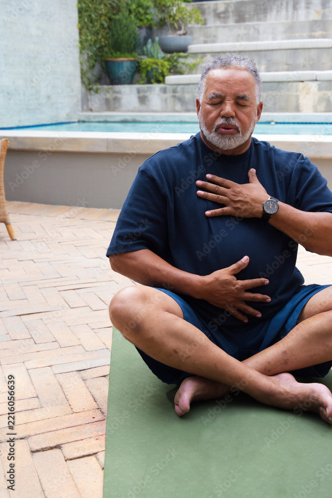 Naklejka premium Senior African American man sitting on green yoga mat beside pool wearing navy T-shirt and watch