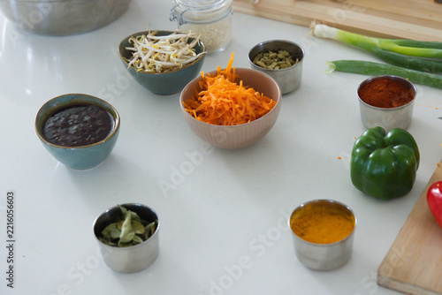Pink ribbed bowl holding shredded carrots is sitting on white countertop near teal bowls and spices