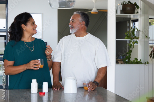 African American couple standing at kitchen island holding glasses of orange juice, pill bottles