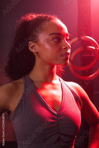 African American woman in her twenties training in fitness studio wearing grey tank top, gym rings