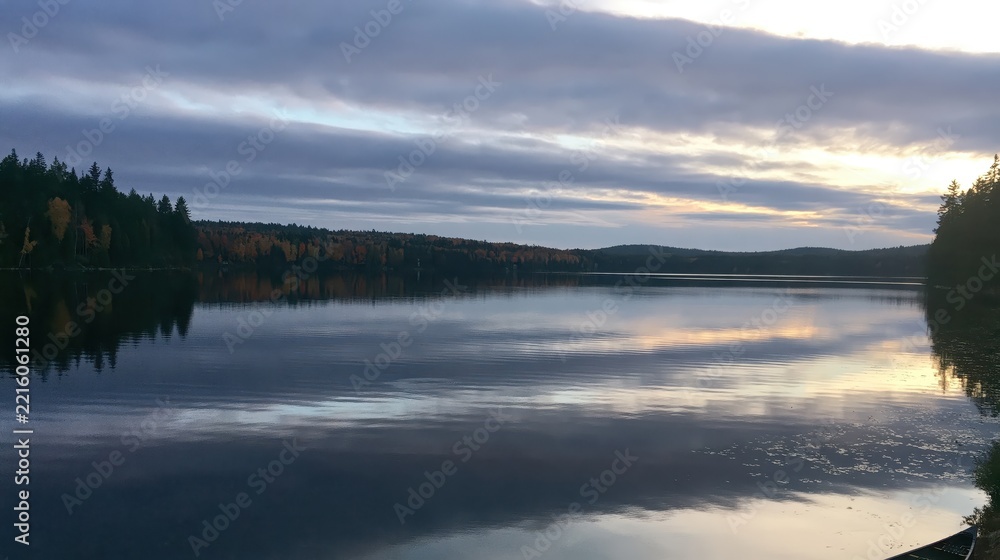 Fototapeta premium Calm lake reflecting autumn forest and cloudy sky at dusk