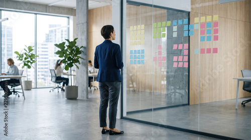 Office worker planning security strategy beside glass wall covered with notes, while modern firewall protects business data.